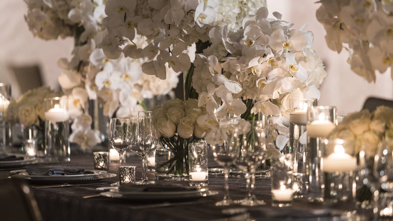 White orchid flowers in centre of long dining table with glowing candles