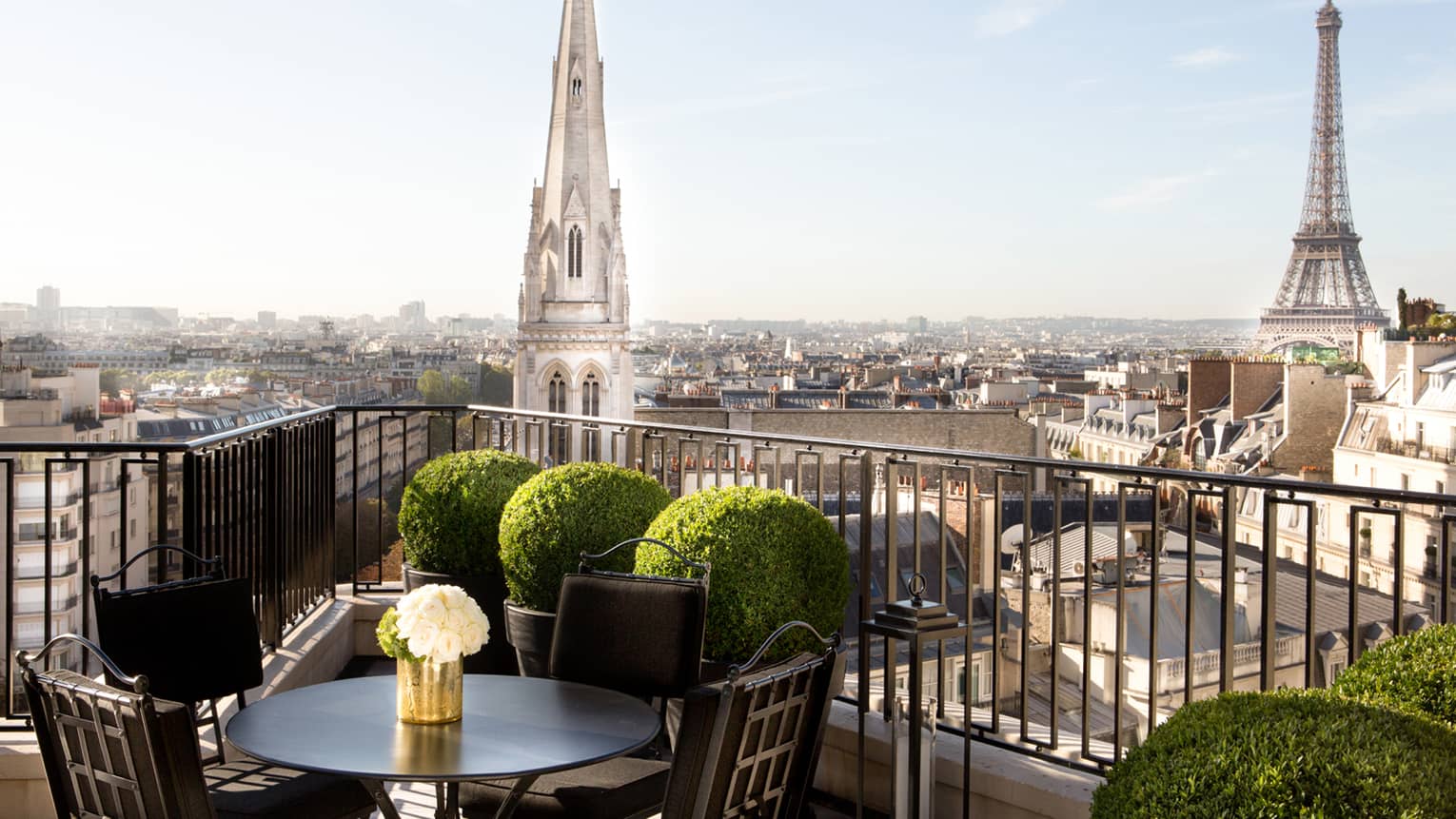 Patio dining table with white roses, potted shrubs iron balcony overlooking Paris rooftops, cathedrals