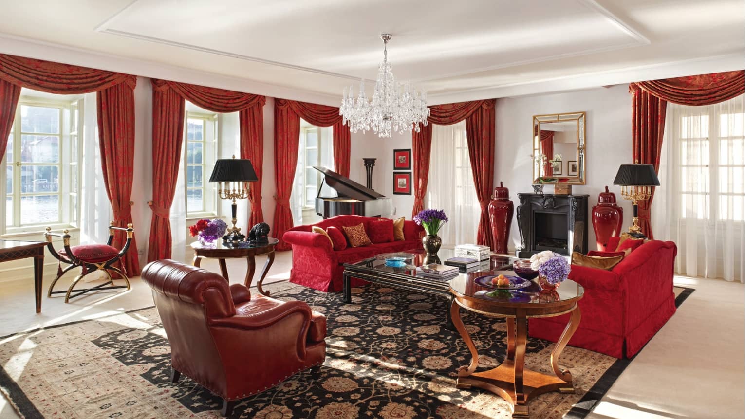 Presidential Suite with red sofas and armchair, red curtains on sunny corner windows, crystal chandelier 