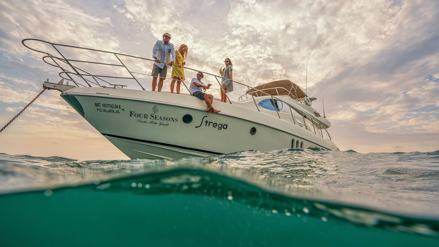 White Four Seasons motor yacht anchored in ocean, two men and two women look out at sea
