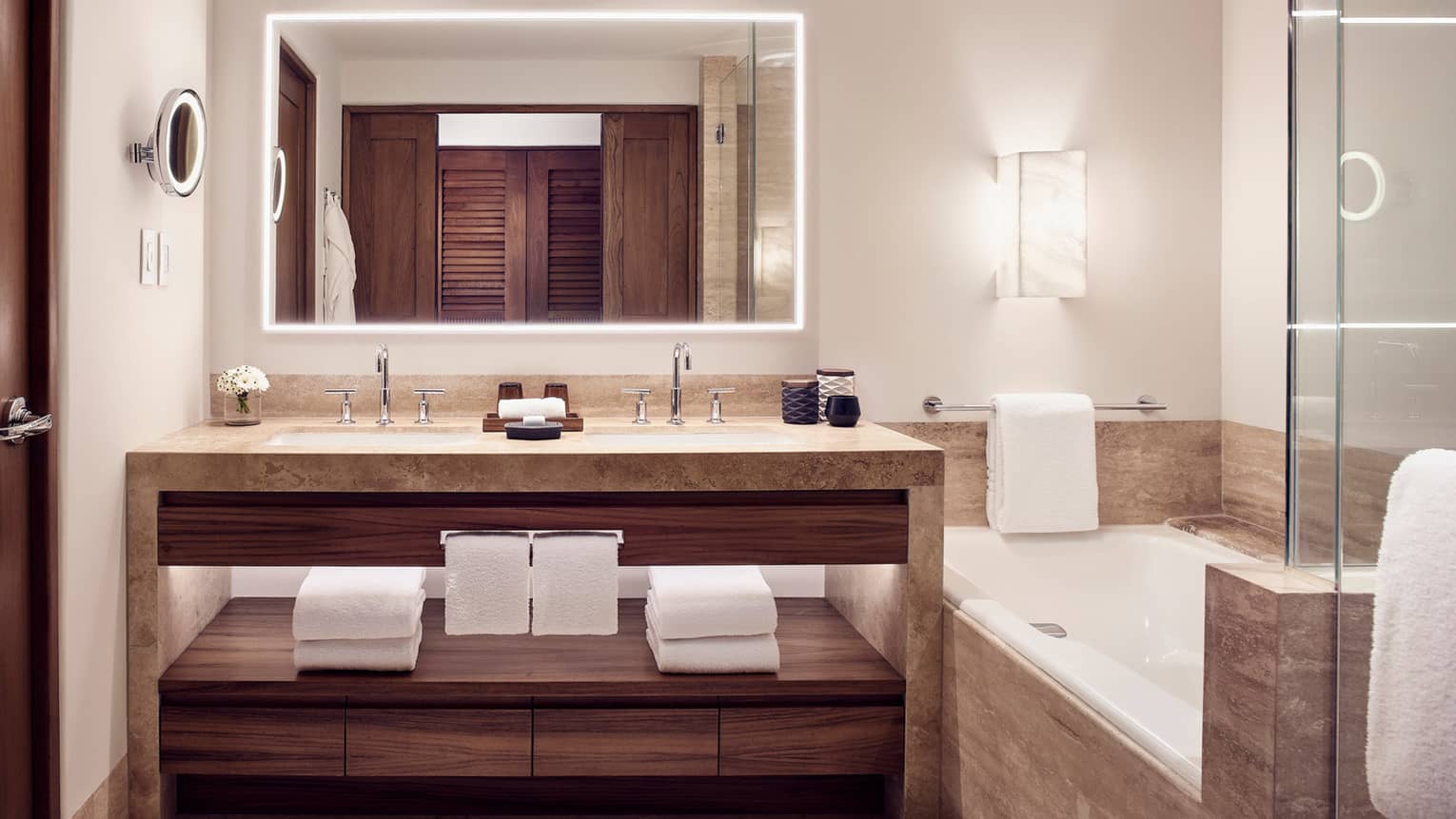Bathroom with light stone double vanity, built-in tub, illuminated mirror