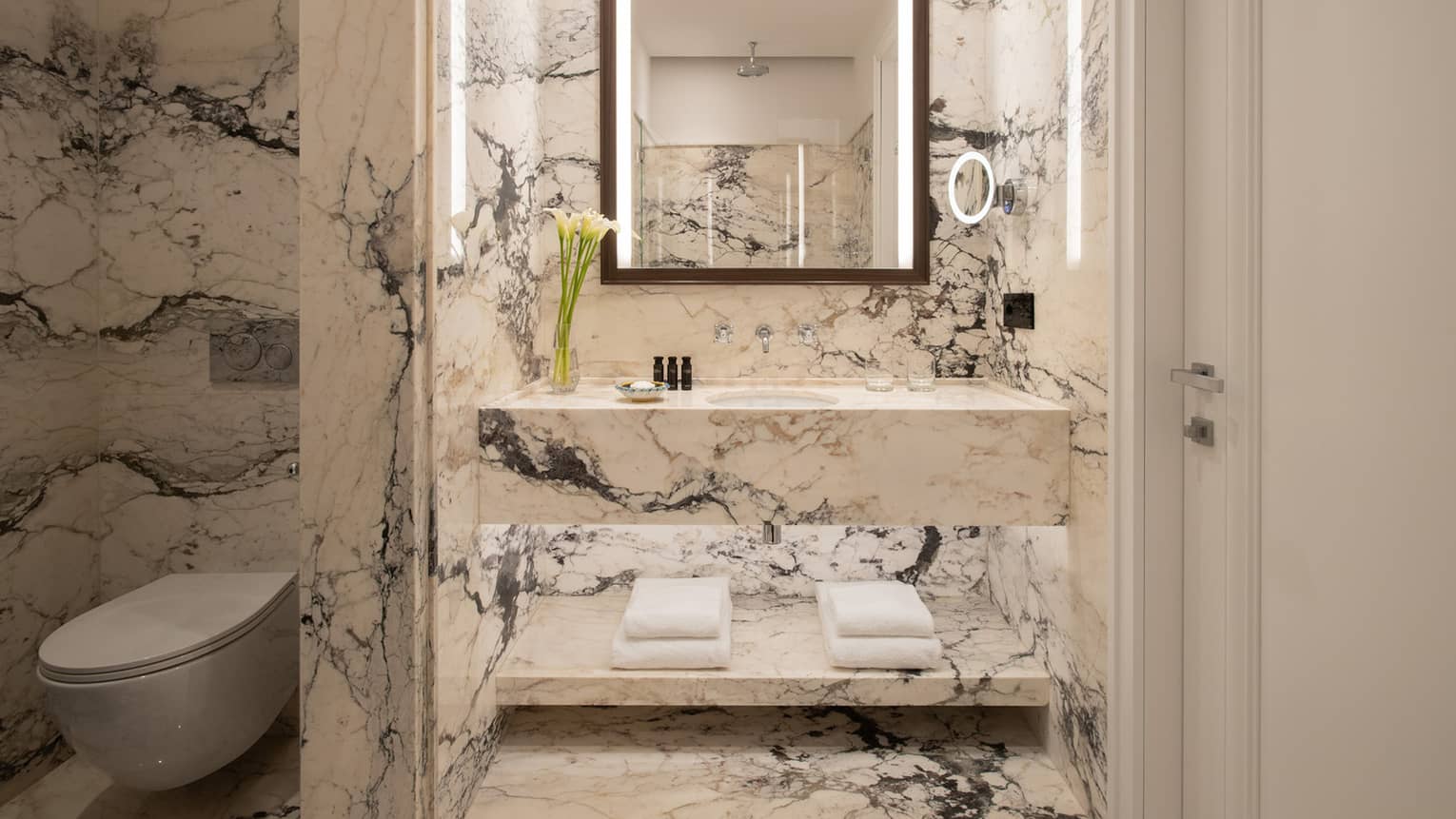 Bathroom with black and white marble walls and vanity, illuminated mirror, separated toilet room