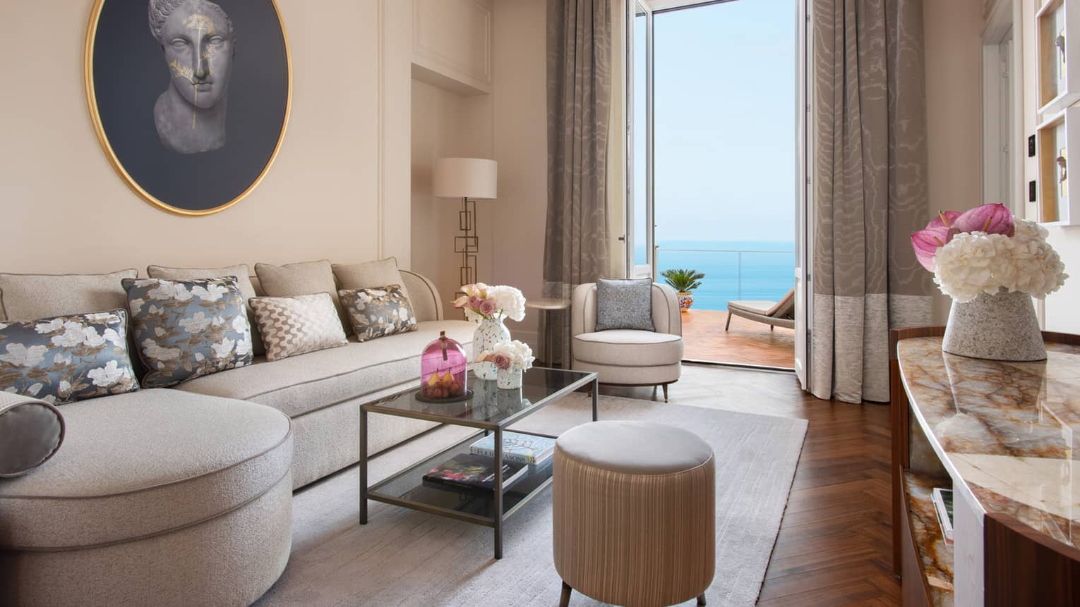 Living room with curved, taupe-coloured sofa, doors leading to ocean-view balcony