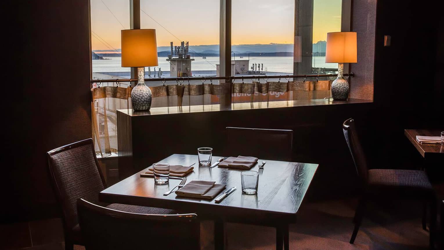  Goldfinch private dining table near sidebard with two lamps, window overlooking water at sunset