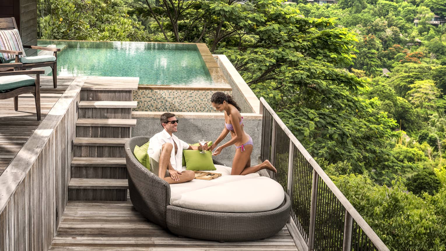 Man and woman wearing swimsuits lounge on large patio chair on deck under plunge pool