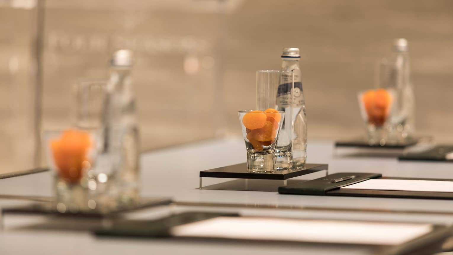 Close-up of meeting table place setting with agenda, dried apricots in glass, bottle of sparkling water