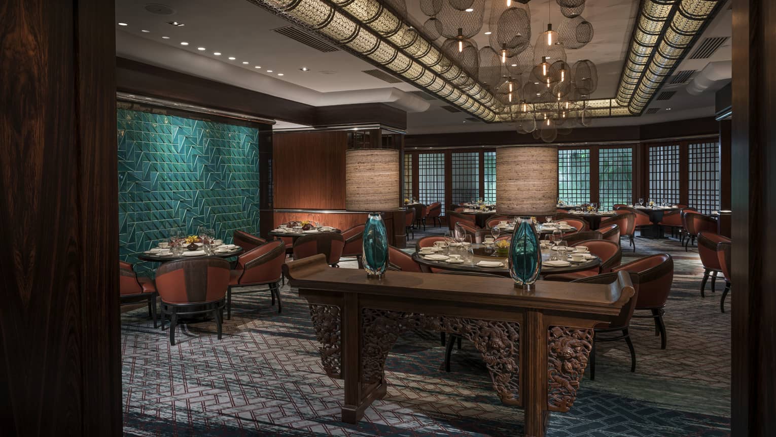 Carved wood console with glass vases in front of dining room, green tile wall