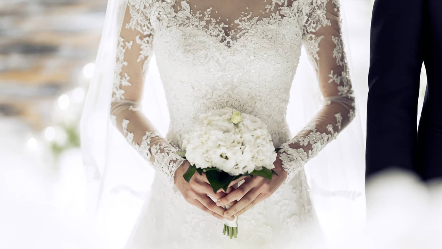 Close up of bride wearing white lace wedding gown and holding bouquet 