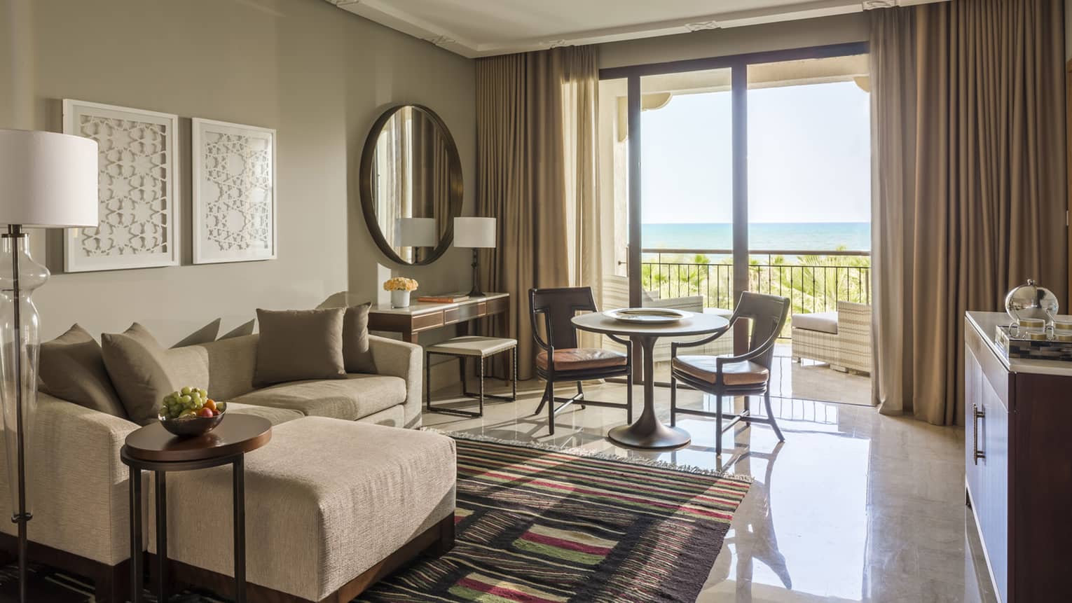 Deluxe Sea View hotel room with modular sofa, small table and chairs by sunny balcony doors