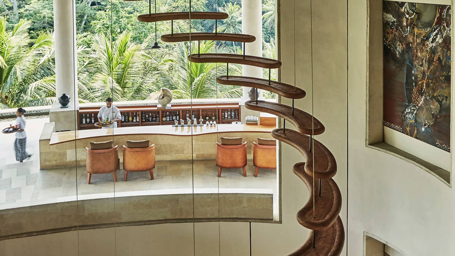 Winding staircase with curved, floating stairs, glass wall looking out at sunny Jati Bar patio, bartenders 