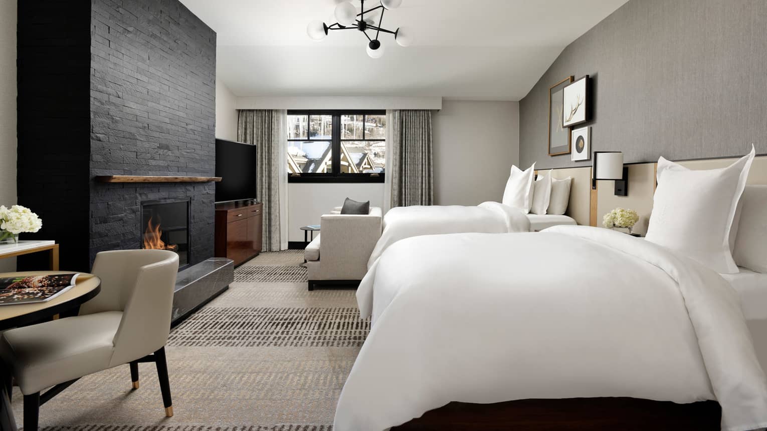 Hotel room with grey walls, black stone fireplace, two white double beds, arm chair