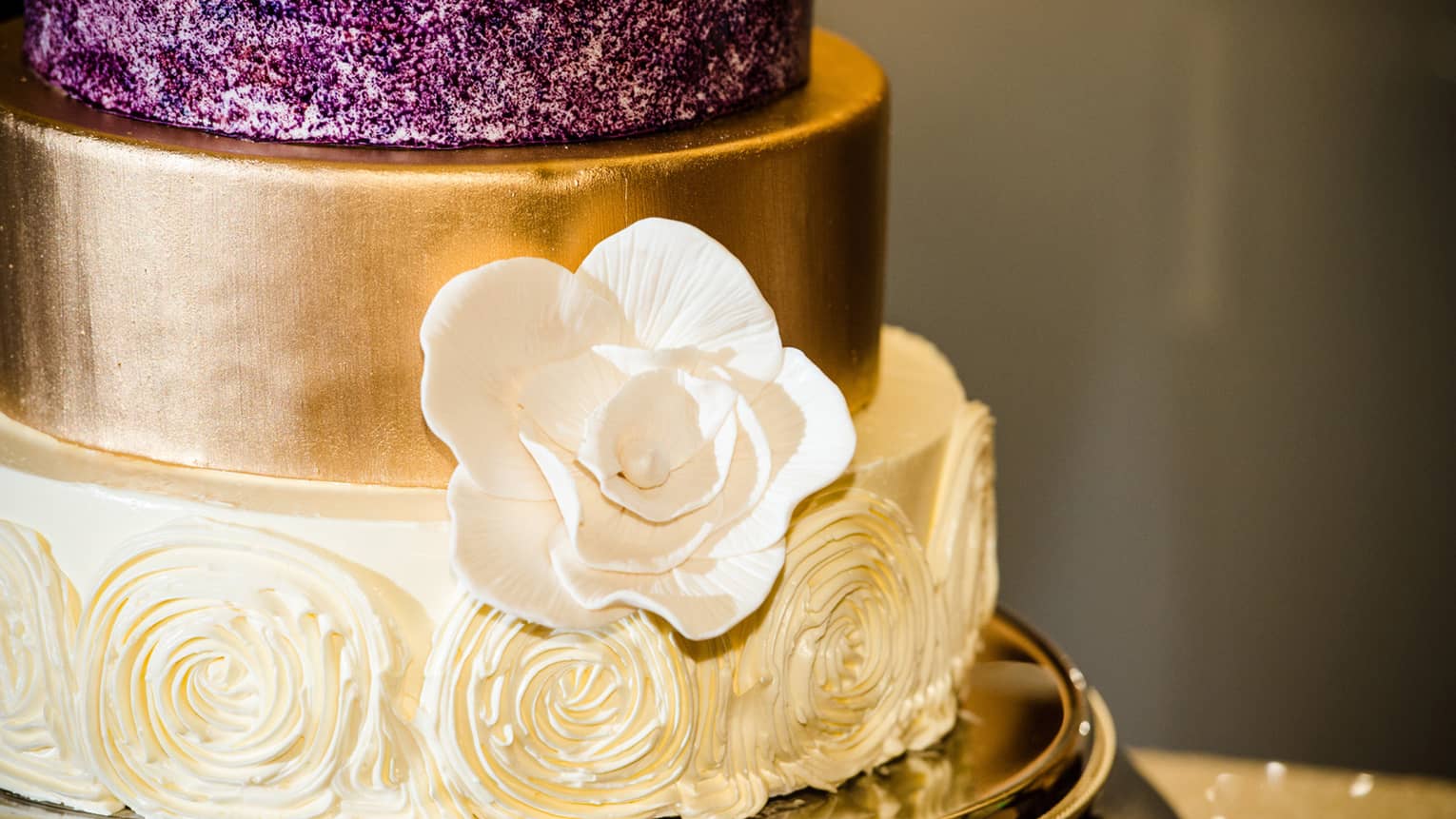 Wedding cake with purple, gold and white tiers decorated with icing flowers