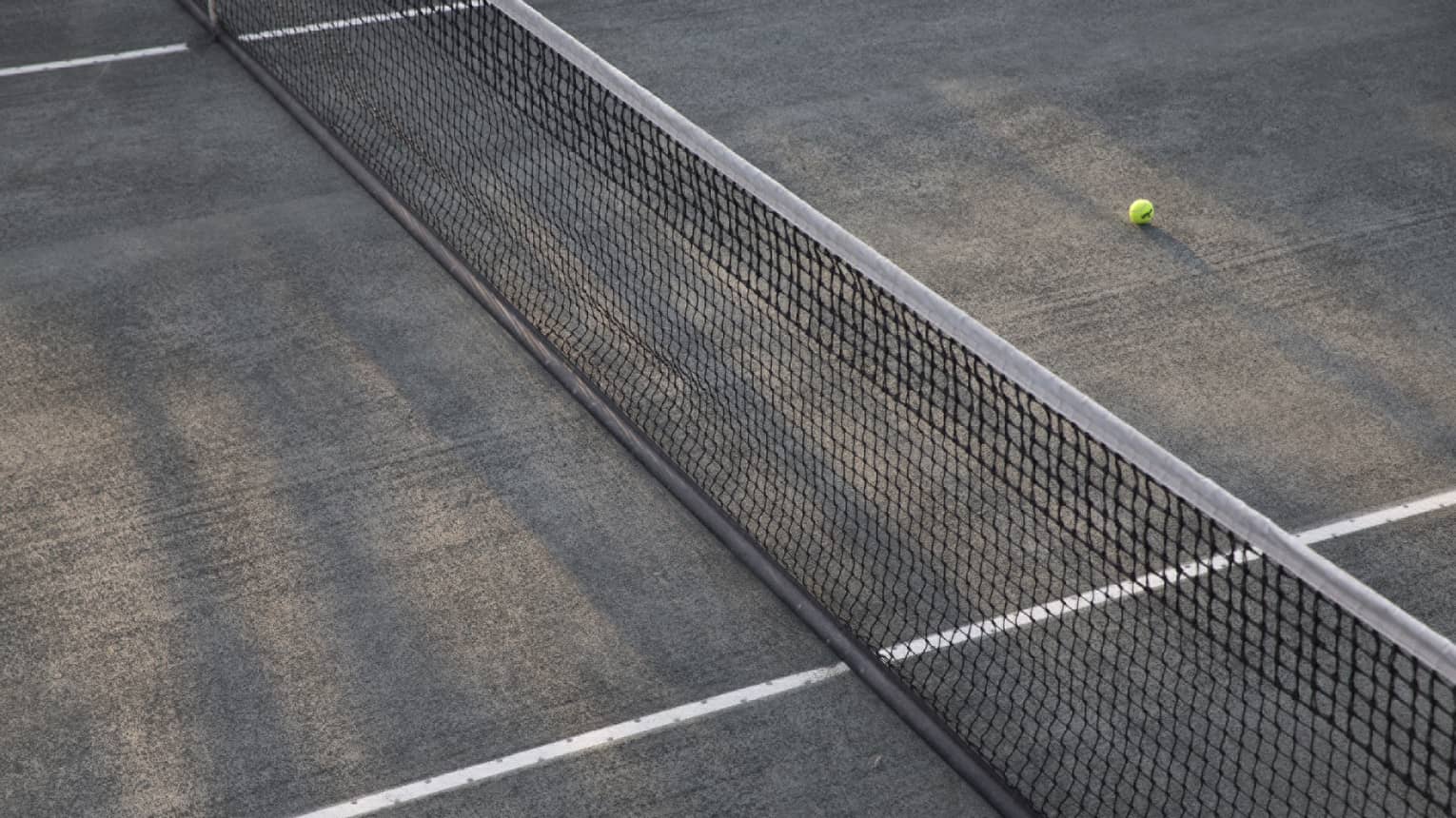 A lone tennis ball lies near the net on an empty court