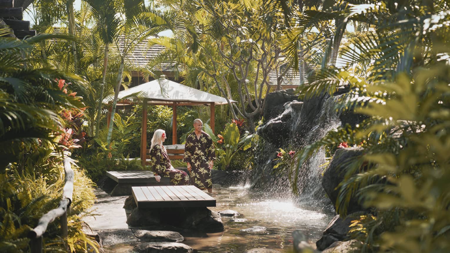 Two four seasons guests lounge in robes at the lush, vegetation-surrounded outdoor spa