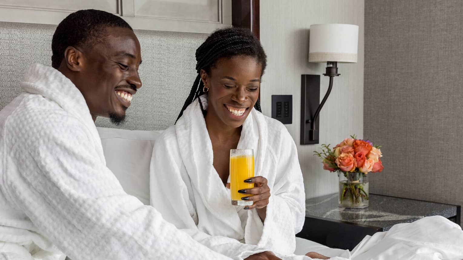 ,A couple dressed in white bath robes enjoys breakfast in bed
