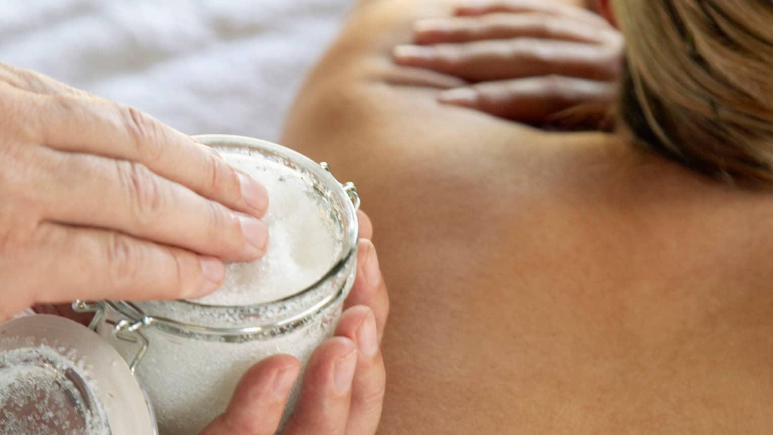 Jar of sea salt scrub above woman's bare back in spa