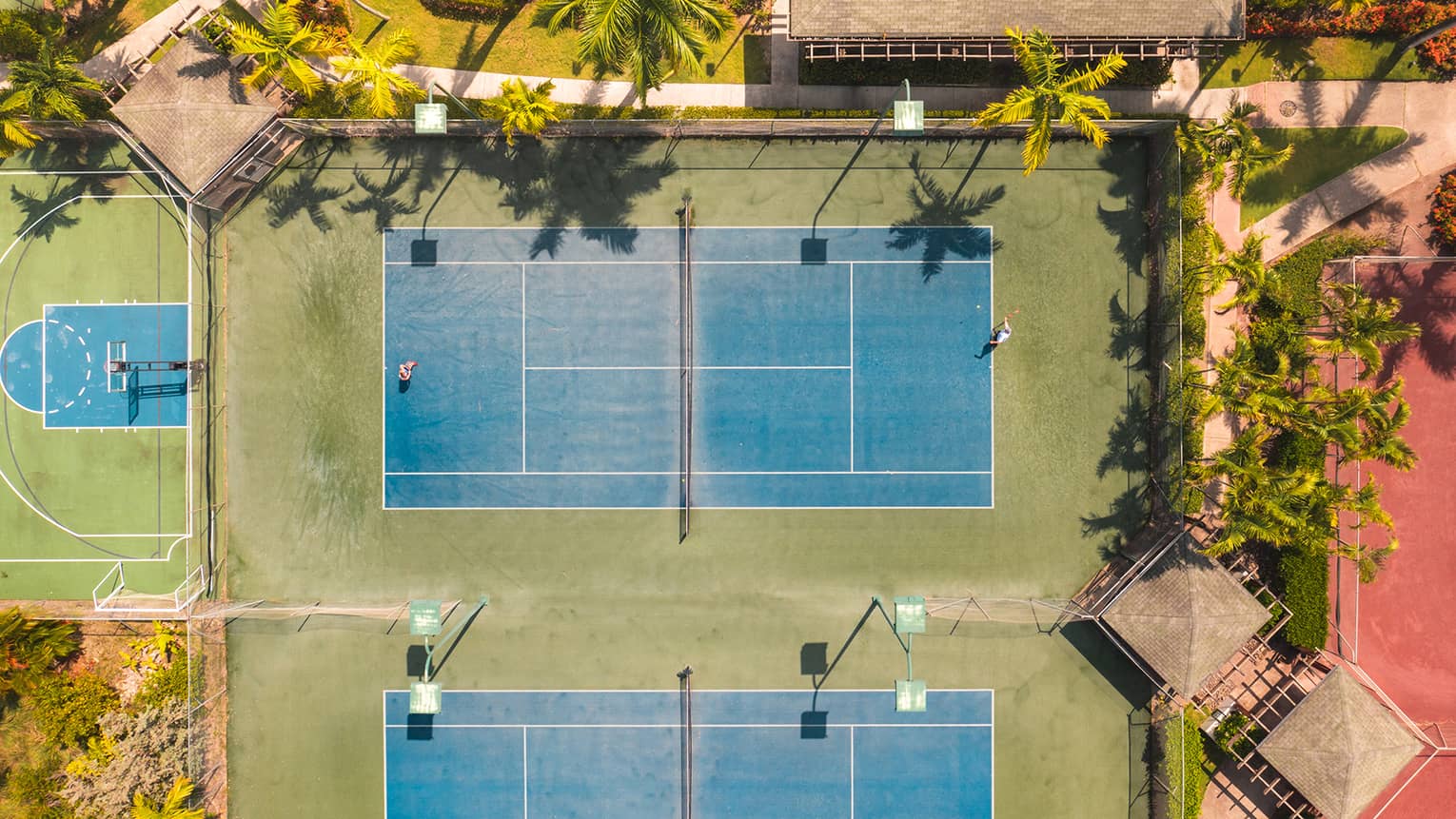An aerial view of tennis courts surrounded by palm trees.