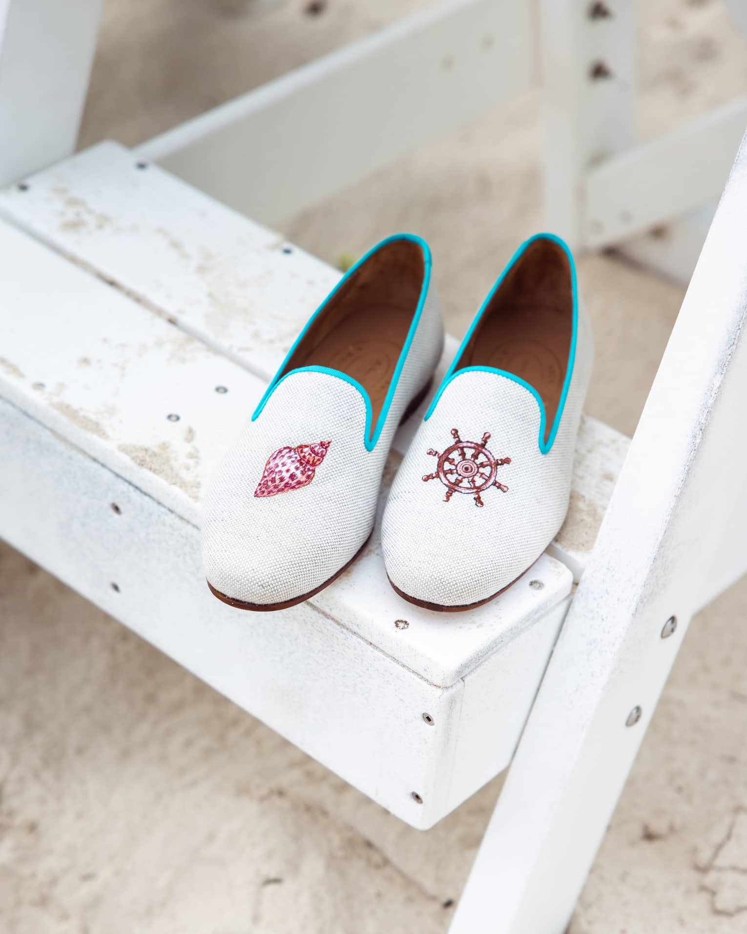 A pair white and blue shoes with a symbol of a seashell and of a boat wheel on each.