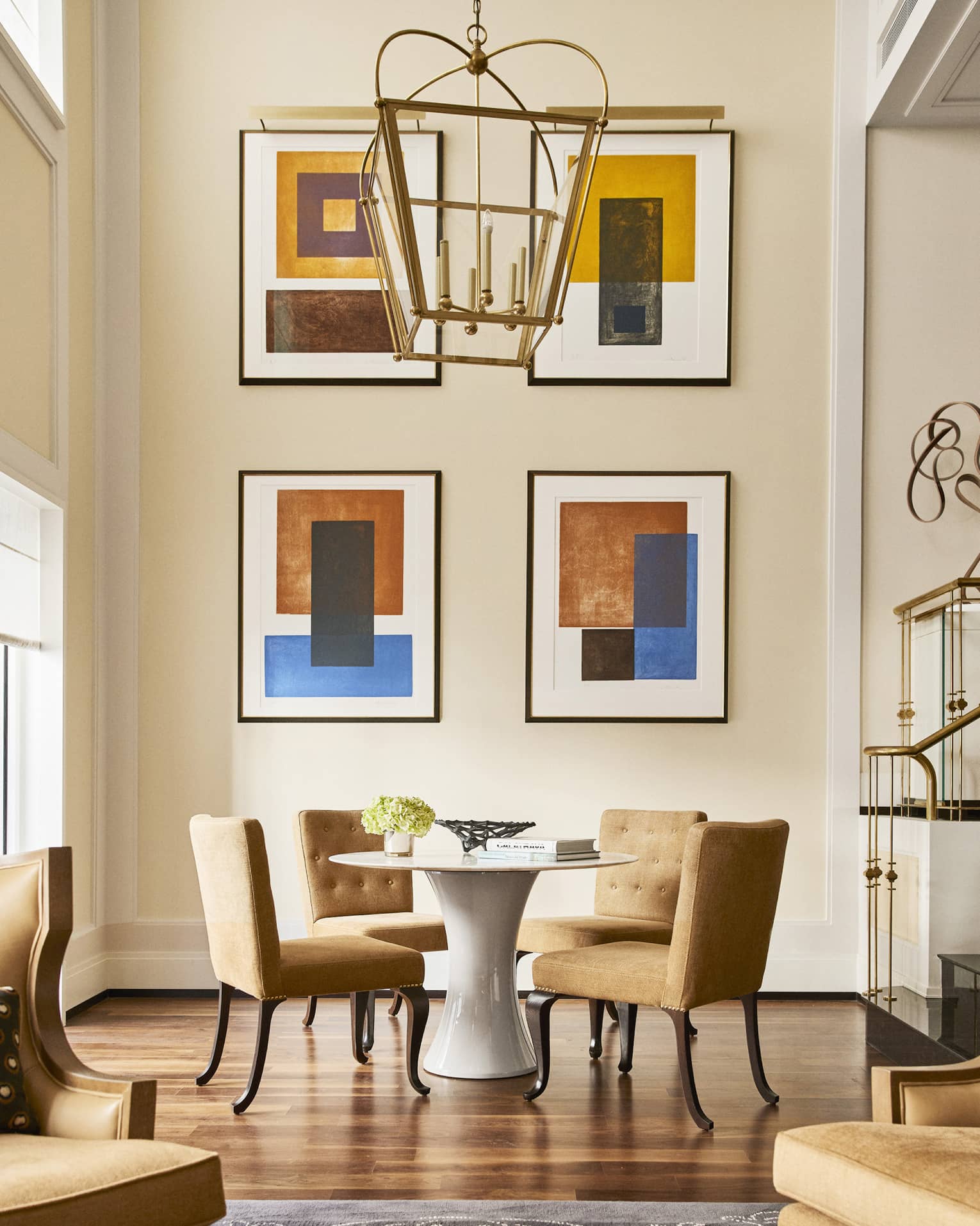 Round table with four brown upholstered chairs beside tall wall with four abstract art pieces