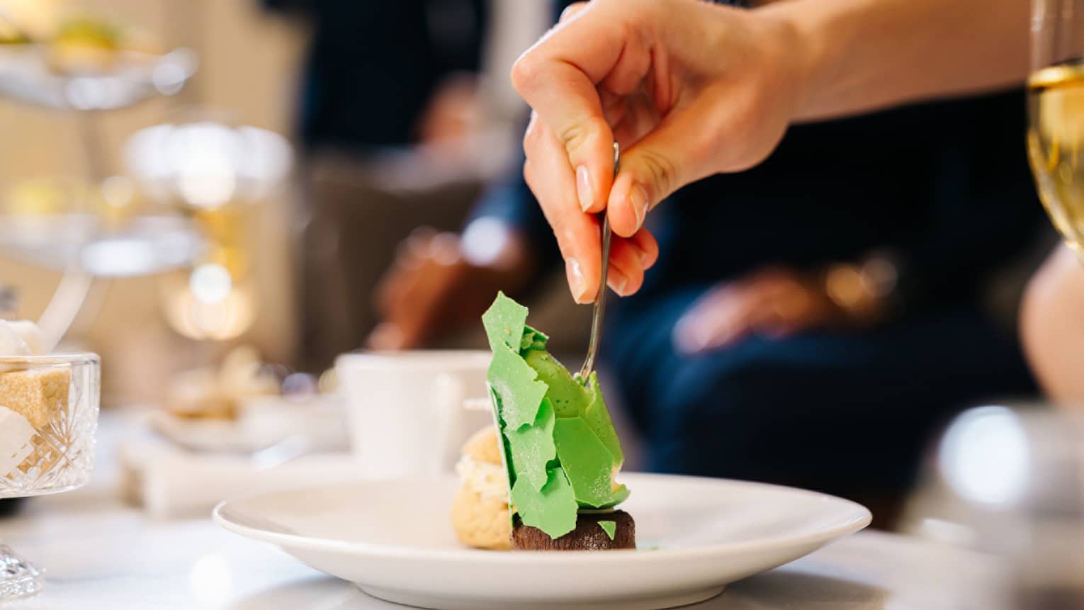 A person putting a fork into a small pastry during afternoon tea.