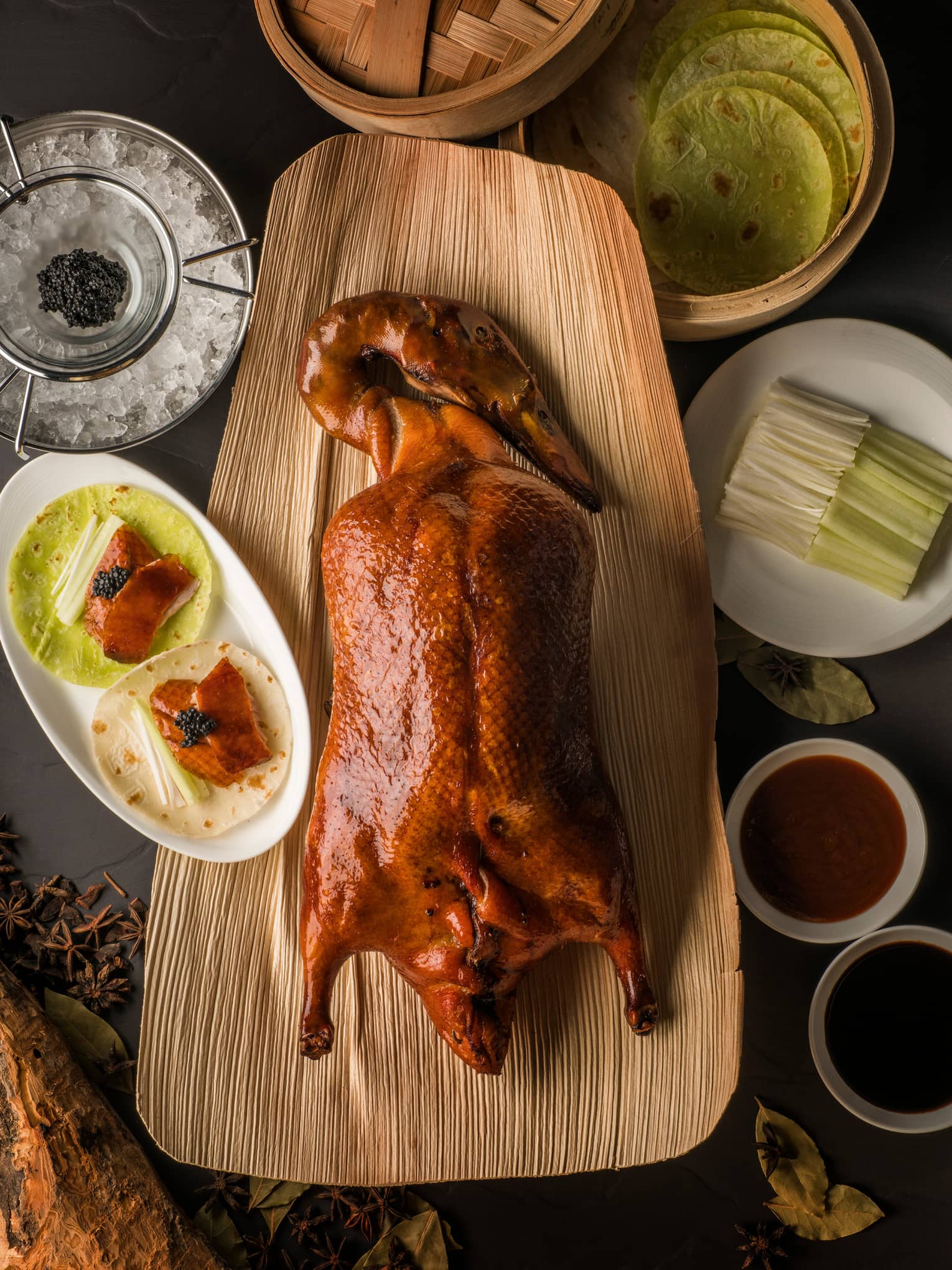 Aerial view of whole Peking duck on wood platter beside small dishes with slices