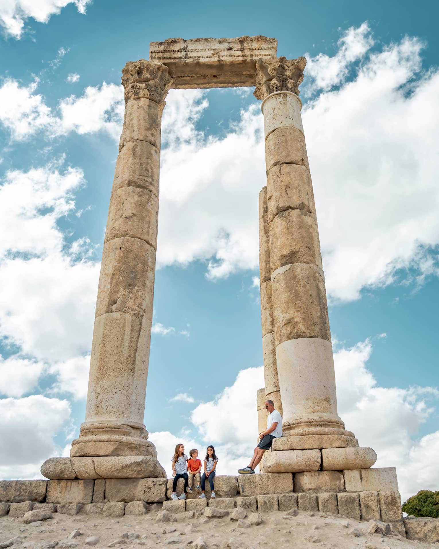 A family sitting in the center of a set of stone pillars in front of a blue sky.
