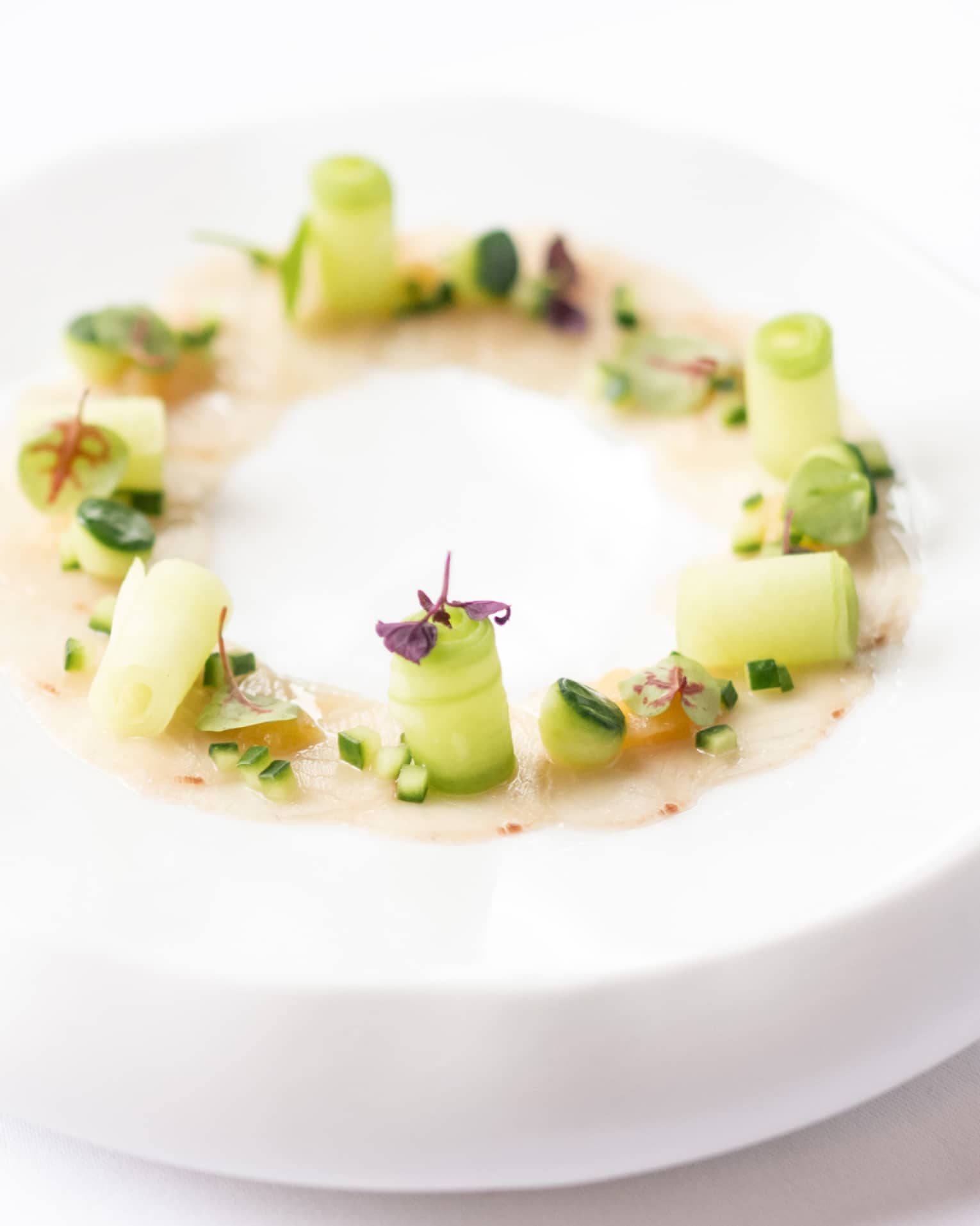 Round white dish topped with green vegetables and a light pink sauce