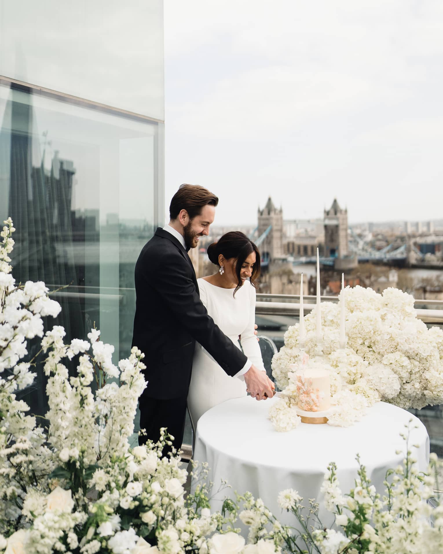 Groom and bride cutting the cake together on a terrace with Tower Bridge in backdrop