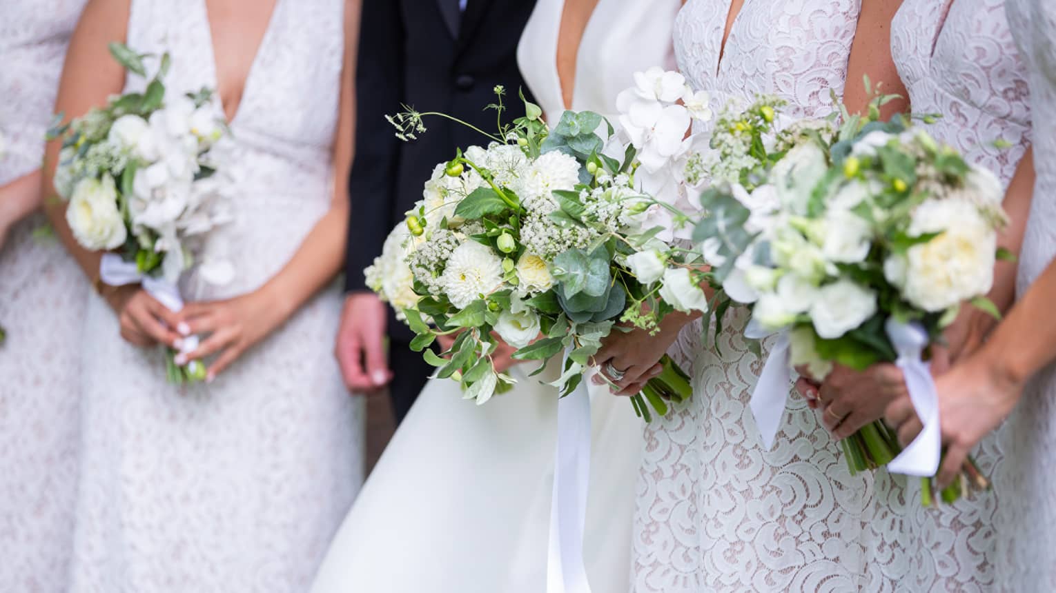 Bride and bridesmaids all wearing white, holding floral wedding bouquets