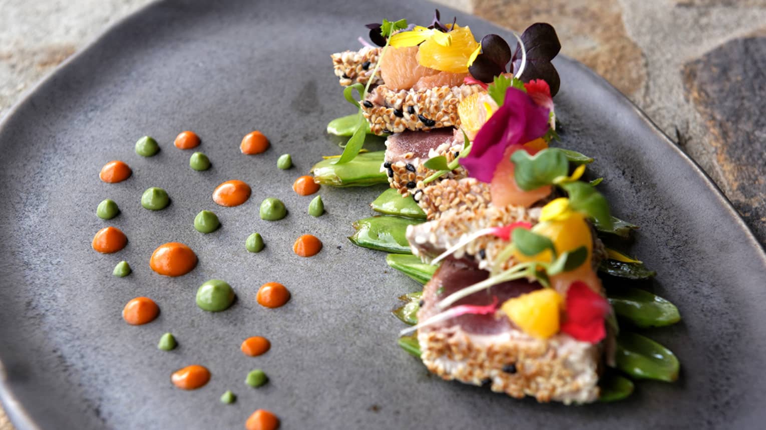 Sesame-crusted tuna topped with colourful edible flowers and green & orange dots