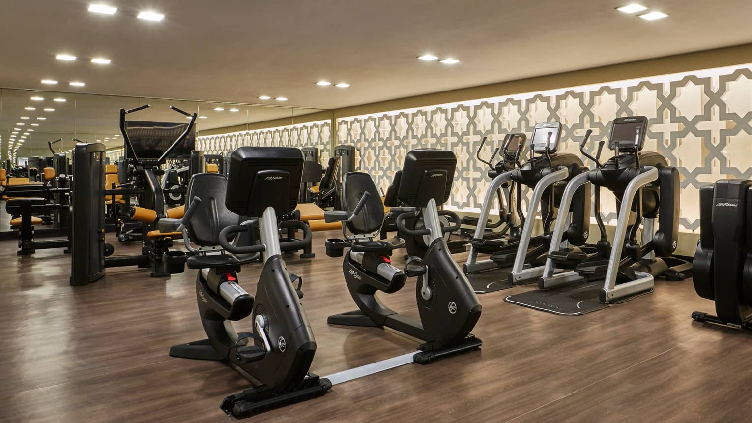 Rows of cardio machines in dimly-lit fitness room with wood floors