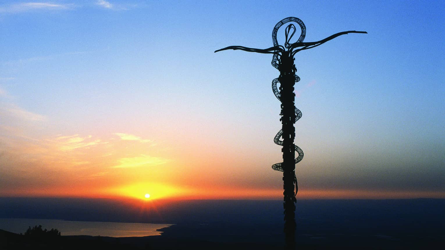 A cross-like statue rises above the horizon at sunset at Mount Nebo