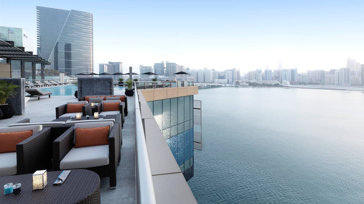 Rooftop lounge with stylish black wicker armchairs, cushions, candles on tables, swimming pool, overlooking Arabian Gulf
