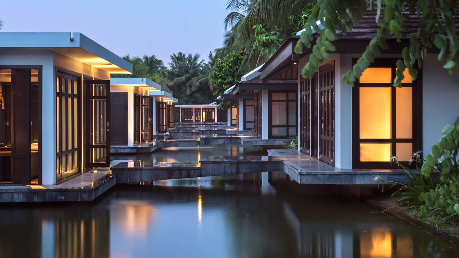 Spa villas over lotus pond connected by marble tile walkways at dusk
