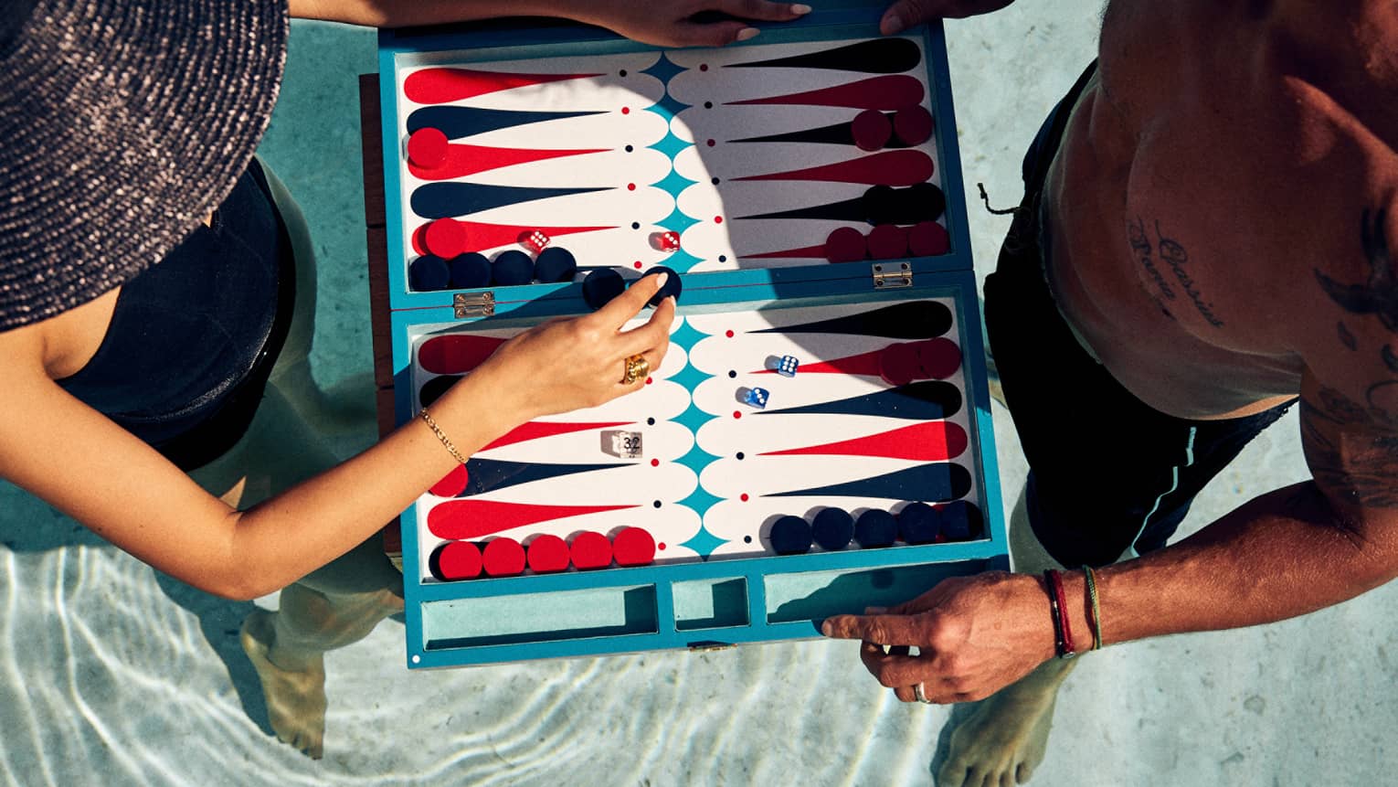 Aerial shot of man and woman in a pool, playing a floating game of backgammon