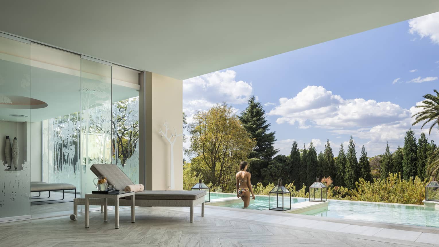 Woman walks into outdoor plunge pool in front of covered patio with chaise 