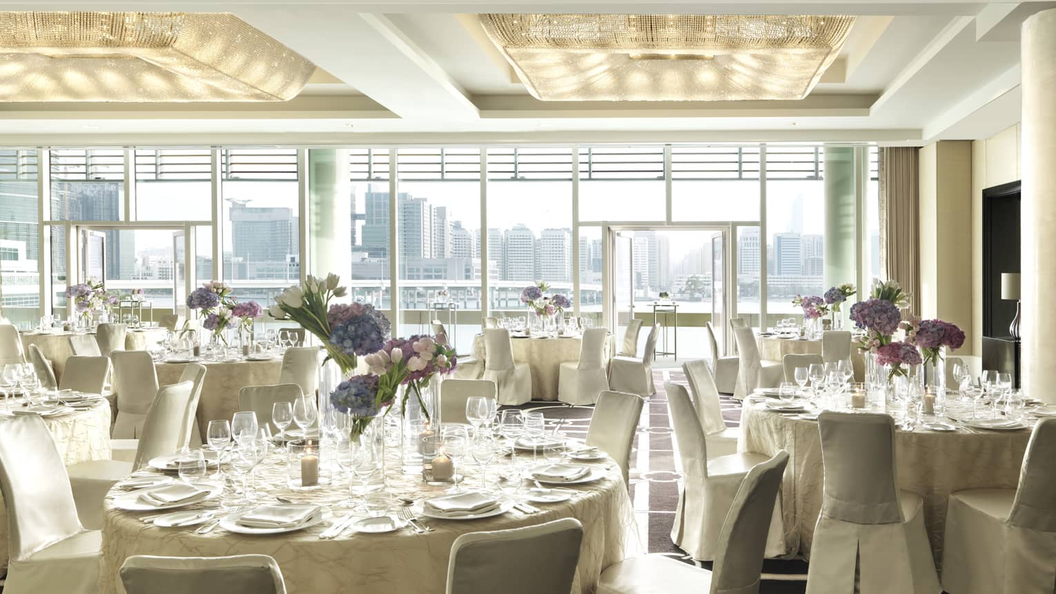 Sunny Liwa Ballroom with floor-to-ceiling window, round banquet tables with white linens, chairs 