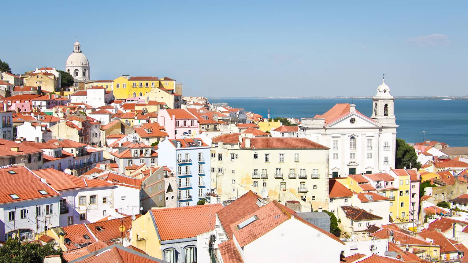 Aerial view of Lisbon skyline and rooftops on sunny day white houses, apartment buildings with brown roofs, white church