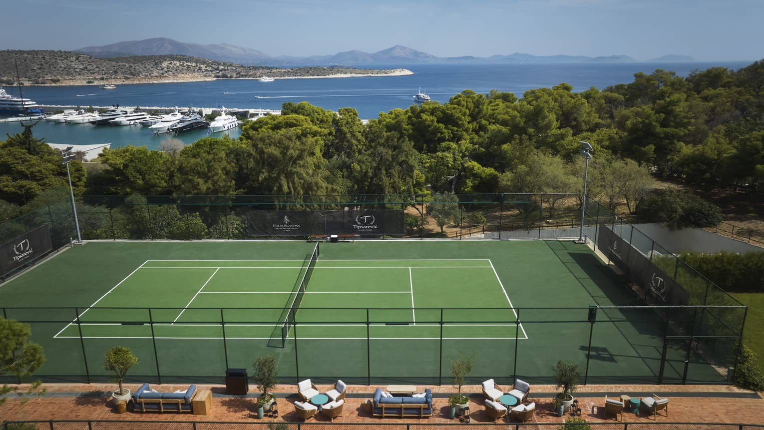 A tennis court with a forest and oceans in the background.