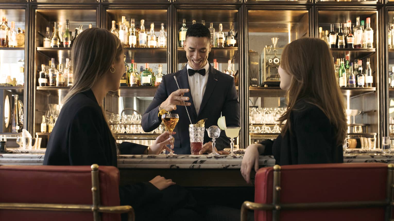 Two women sitting at a bar being served by a bartender.