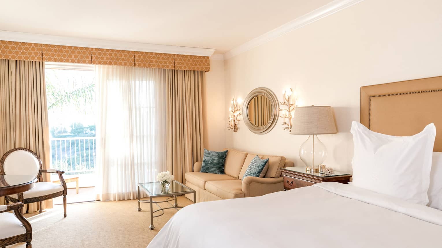 Hotel villa bedroom, bed and seating area by sunny floor-to-ceiling patio door 