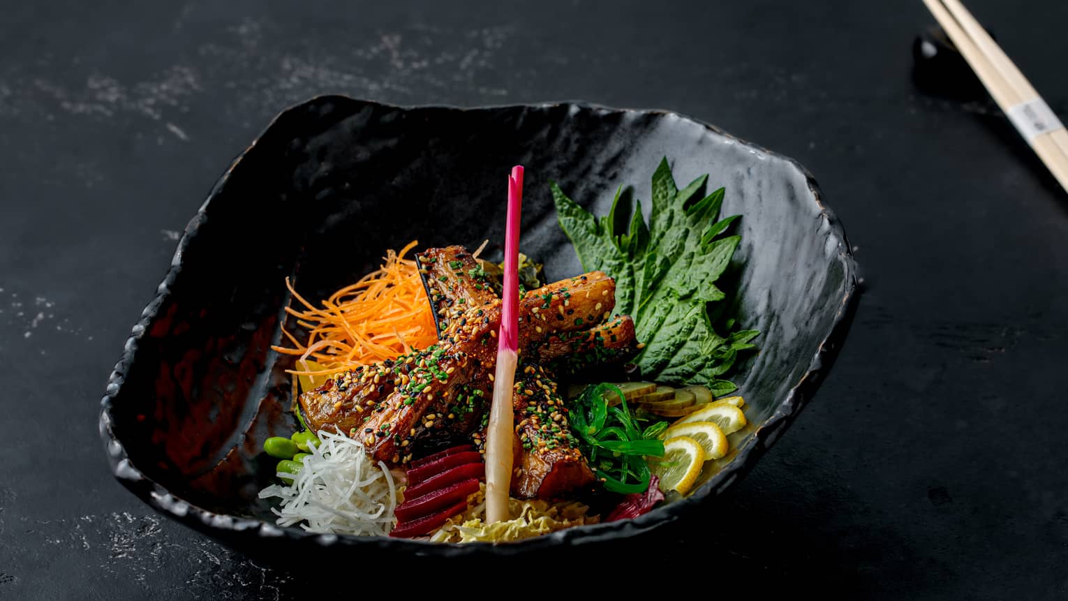 A black bowl filled with salad, edamame, mushrooms and a vinaigrette.