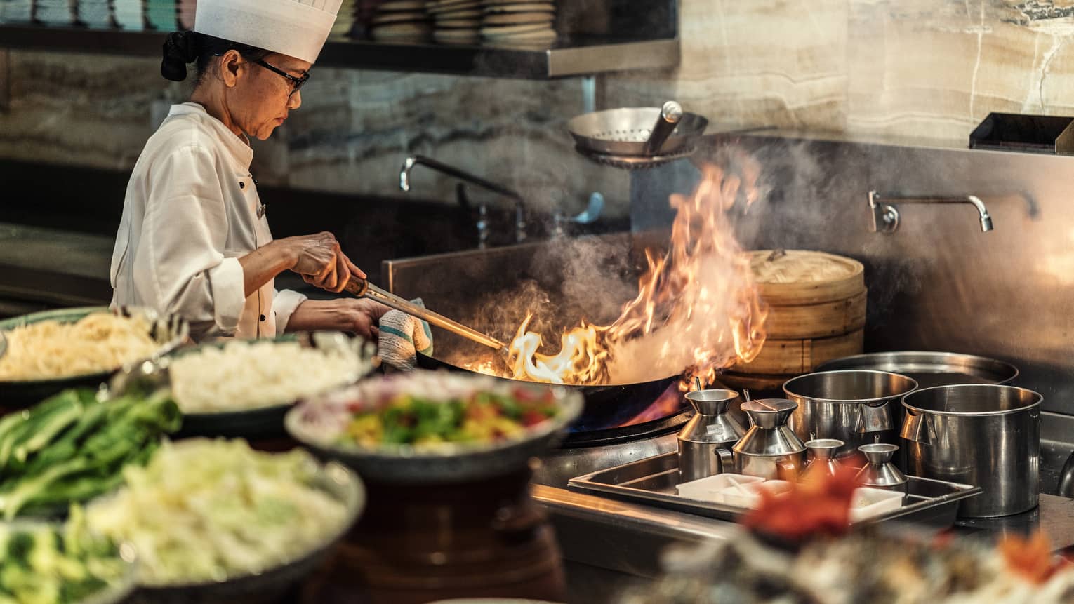 A four seasons chef sautees something with a large flame in the kitchen 