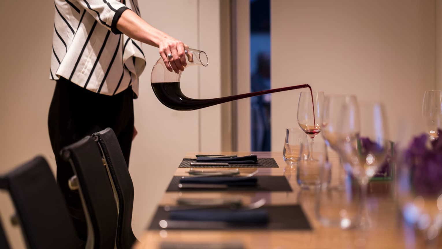 Close-up of woman in striped jacket pouring red wine into glass on meeting table