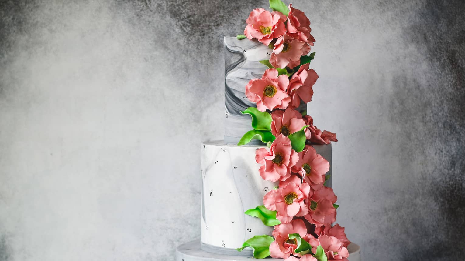 Three tiered wedding cake with marble icing design, decorated with cascading pink flowers