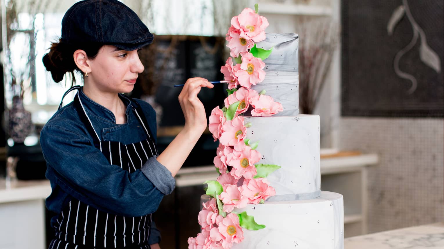 Chef places large pink flowers on three tiered wedding cake