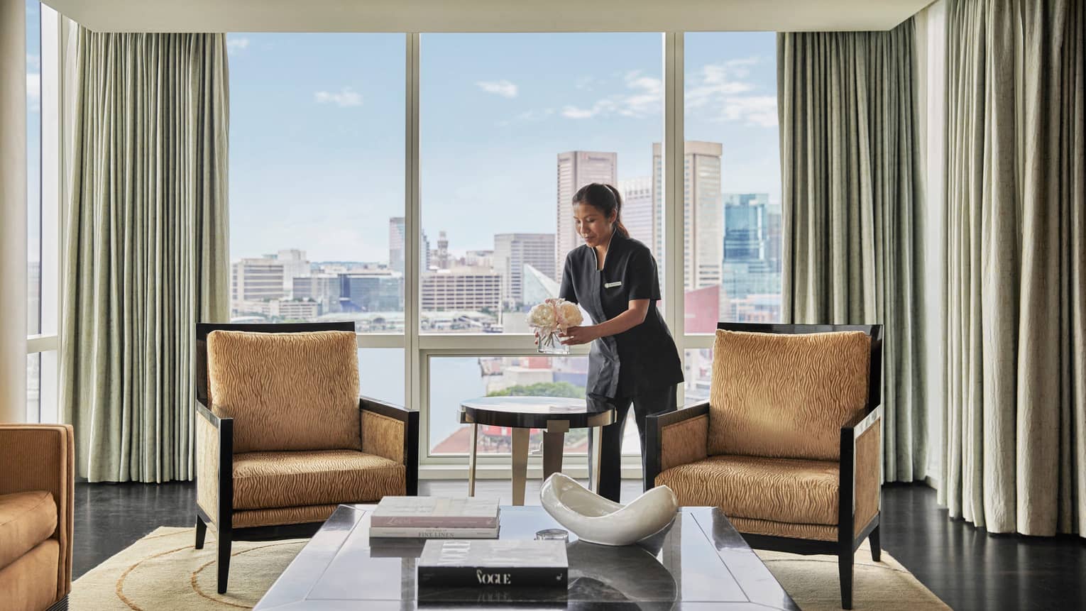 Woman cleaning a living room, with four gold-coloured, upholstered arm chairs, large coffee table