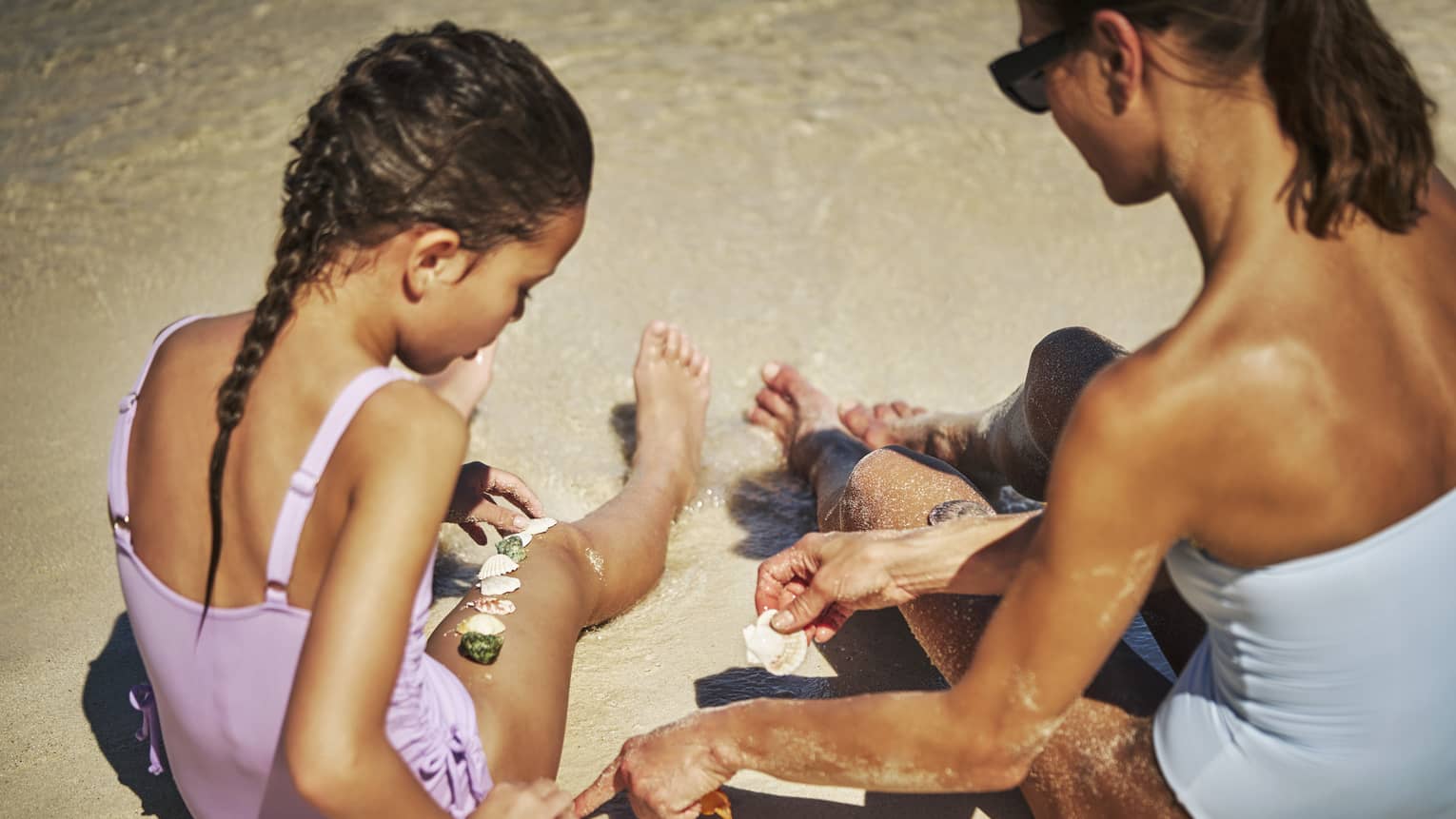 Mother and daughter finding shells in the sand on the beach.