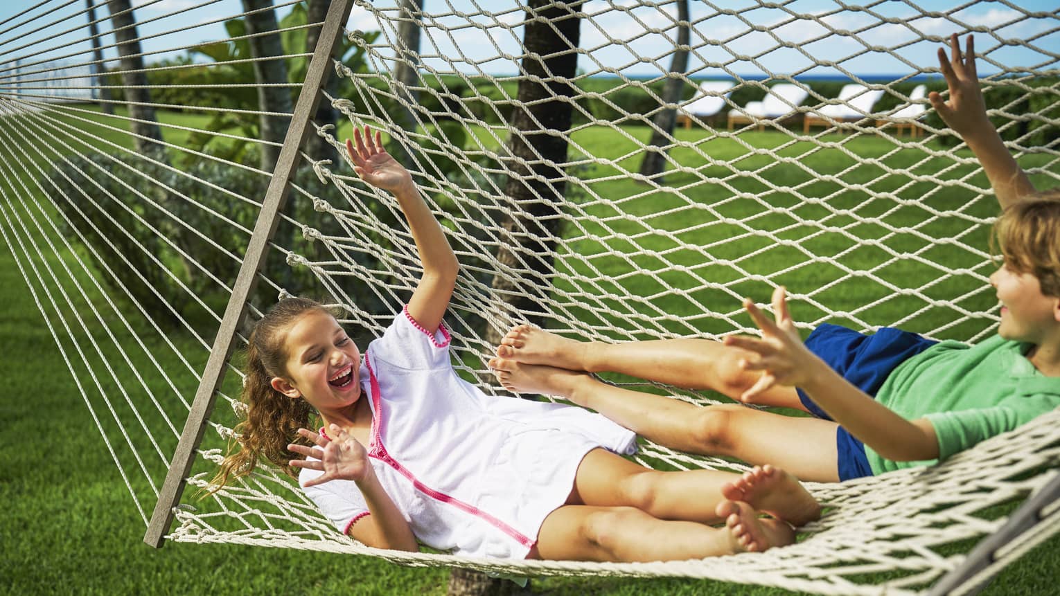 Two children swinging on a hammock outside.