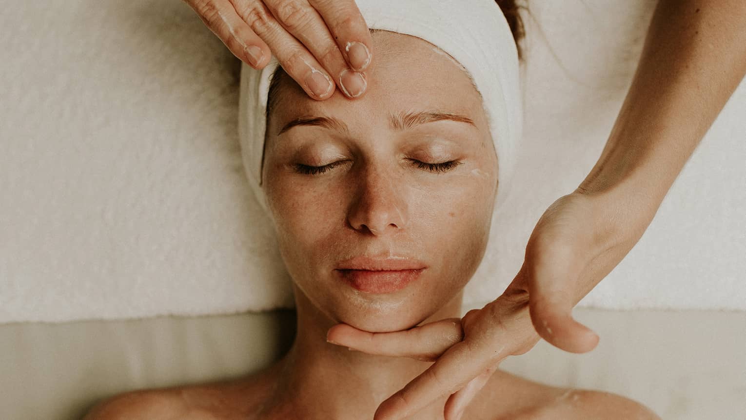 A woman reclines as a spa attendant performs a facial